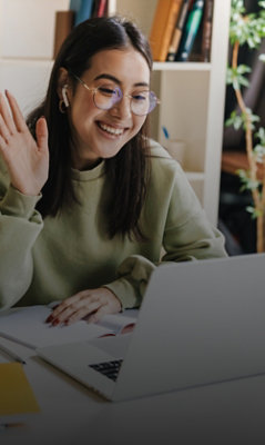 Person wearing glasses waving during a video call while using a laptop at home.
