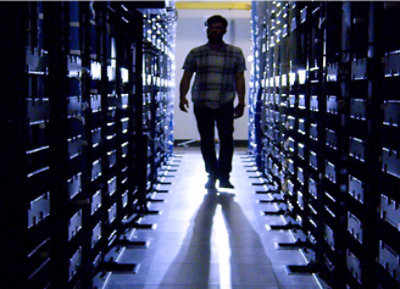 Мужчина в клетчатой ​​рубашке идет по серверной.