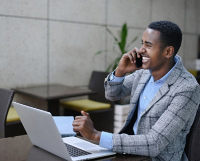 Man sitting infront of laptop and talking in mobile and laughing.