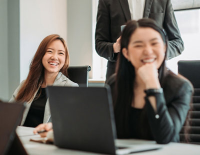 Two womens sitting infront of laptop looking side and laughing with one women face blurr