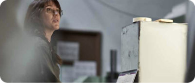 People in a conference room are working on computers with data displayed on screens in the background.