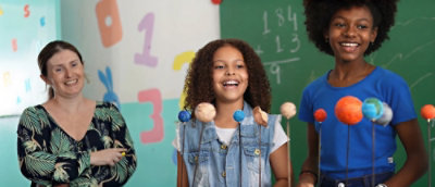 Teacher and students smiling while viewing a model of planets in a classroom.