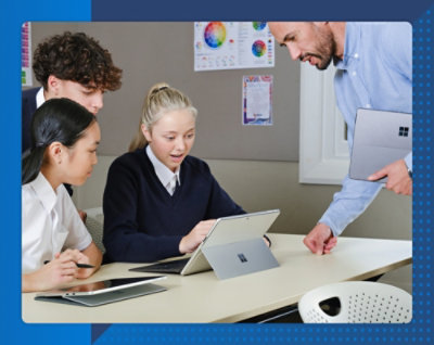 Teacher helping students use a tablet together at a desk in a classroom.