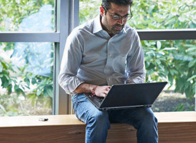 A man sitting on a window sill using a laptop.