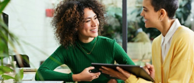 Two people are discussing, and a woman in a green shirt with short curly hair is smiling.
