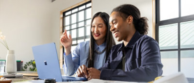 A man and woman are smiling together while looking at a laptop.