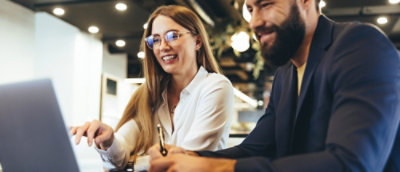 A man and a woman are smiling while looking at a laptop.