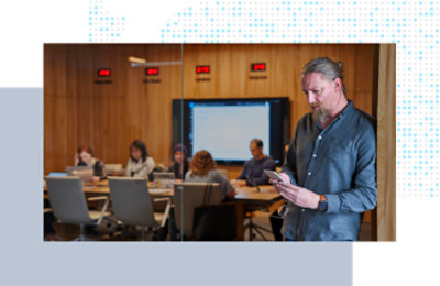 Person checking a mobile phone in a meeting room while others collaborate.