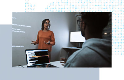 Small group discussion in a workspace, reviewing code displayed on a screen.