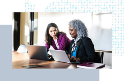 Two coworkers seated at a table, collaborating on laptops during a discussion.