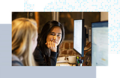 Two coworkers at desks, reviewing information side by side on monitors.