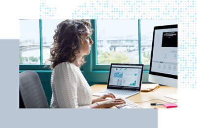 Person working at a desk, viewing charts and data on dual computer screens.