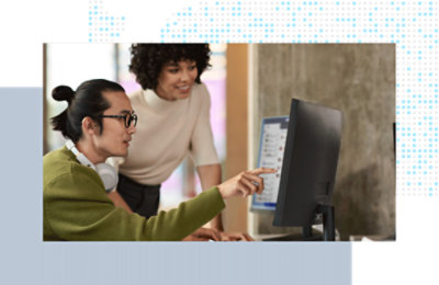 Two coworkers collaborating at a desktop computer, reviewing content on screen.