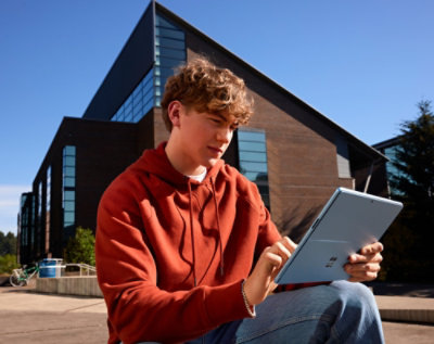 A person using a tablet while seated outdoors near a modern building.