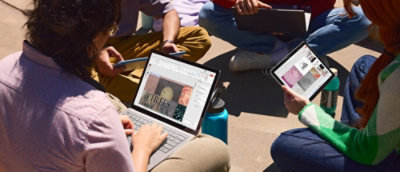 People collaborating outdoors using laptops and tablet devices.