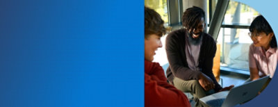 Three people seated together looking at and discussing content on a laptop in a bright indoor workspace.