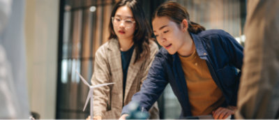 Ofis ortamında masa başında küçük bir rüzgar türbini modeliyle ilgili bir proje üzerinde çalışan iki kişi.