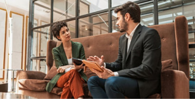 A man in a suit and a woman in a green jacket sitting on a couch.