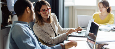 A group of people sitting at a table looking at a laptop.
