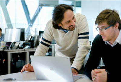 A man wearing glasses and a black sweater looking at a laptop.