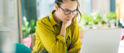 Person wearing glasses working on a laptop in a bright indoor setting.