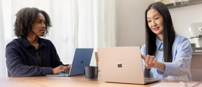 Two people using laptops at a table, one pointing at the screen during discussion.