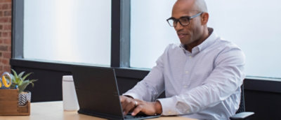 Person working on a laptop at a desk with a water bottle and plant nearby.