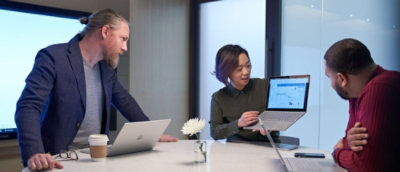 Three people in a meeting, one presenting data on a laptop to the others.