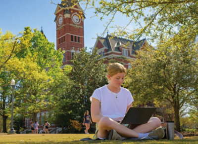 Seorang perempuan duduk di rumput dengan sebuah laptop.