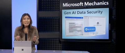 Seorang wanita berdiri di depan layar yang menampilkan Keamanan Data AI Gen Microsoft Mechanics.