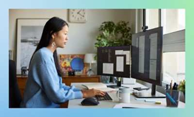A woman seated at a desk, working on a computer with a monitor in front of her, focused on her tasks.