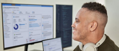 一名男子看著電腦螢幕，脖子上掛著耳機。