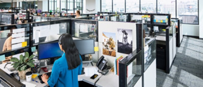 A woman typing on her computer sitting in office desk, surrounded by office supplies.