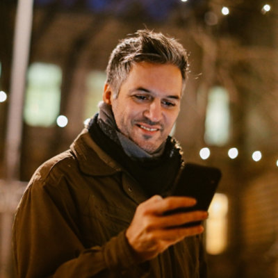 Een man die een bruine jas draagt die naar de telefoon kijkt en glimlacht.