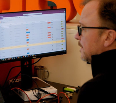 Een persoon die een zwarte jas en een bril draagt die naar het scherm kijkt