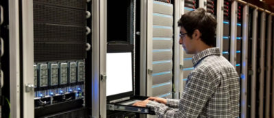 Person working at server rack with keyboard and visible hard drives.