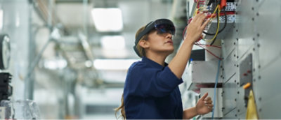 Person wearing augmented reality glasses works on electrical equipment in an industrial setting.