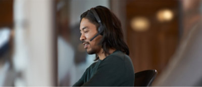 A person wearing a headset sits at a desk, engaged in conversation.