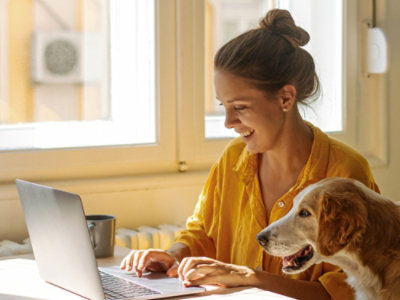 一位穿着橙色衬衣的女士正在使用笔记本电脑，旁边有一只狗