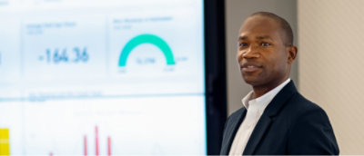 A man in a suit standing in front of a screen displaying -164.36.