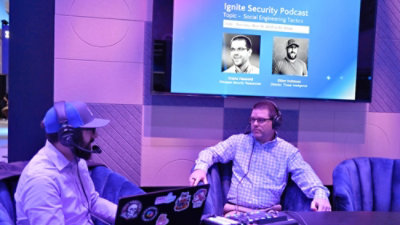 Two men wearing headphones and sitting in chairs with text on a screen in the background that reads Ignite Security Podcast.