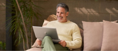 Мужчина держит ноутбук, сидя на диване.