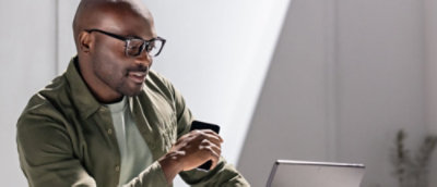 A man wearing glasses and a green jacket looking at a laptop.