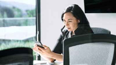 Una persona sentada ante una mesa de conferencia mirando un smartphone