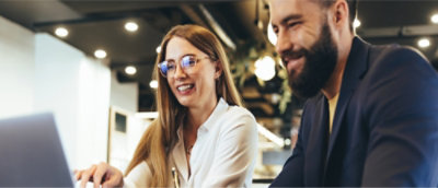 Dos personas sonriendo y mirando la pantalla de un portátil en una oficina.