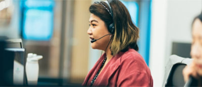 A person wearing a headset sits at a desk, looking at a computer screen.