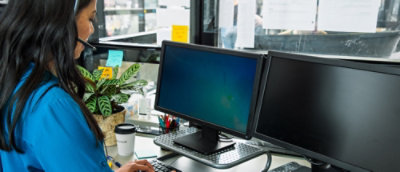 Eine Frau mit Kopfhörern, die an einem Schreibtisch mit einem Computer sitzt.
