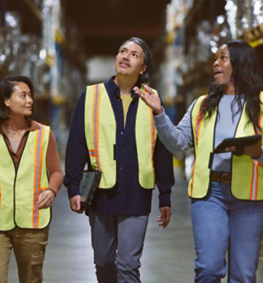 A group of workers walking in a warehouse wearing safety vests.