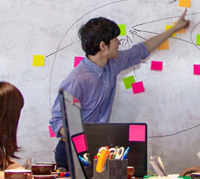 Un homme écrivant sur un tableau blanc avec des post-it collés dessus.