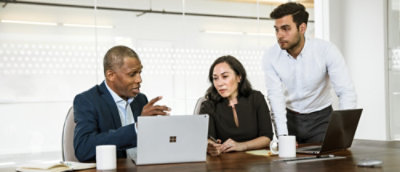 A group of people sitting around a table looking at a laptop.